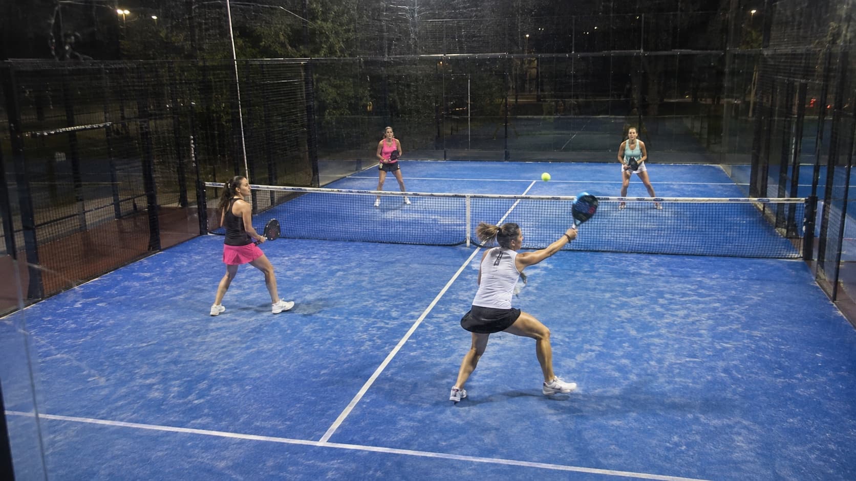Un partido de pádel femenino de noche visto desde la cámara fija, en una esquina alta de la cancha