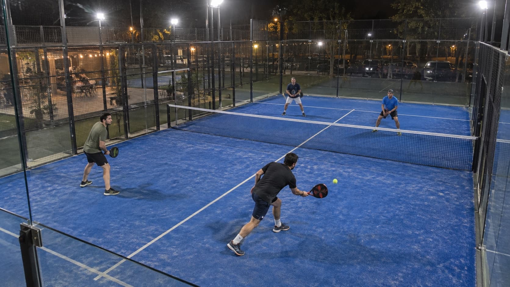 Un partido de pádel de noche en un club de barrio, visto desde la cámara fija de la cancha